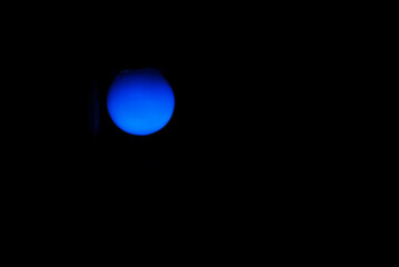 Blue light bulb in the dark, blue moon. Black background with much copy space.