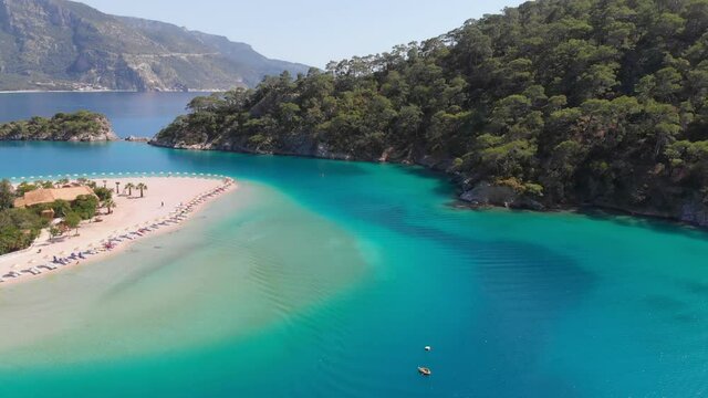 People sunbathe on the sandy beach on the shores of the azure bay. Aerial view of azure water in mediterranean sea in bay near Oludeniz, Turkey. Boat sails through the purest turquoise water
