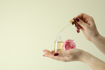 Female hands hold rose essential oil on beige background