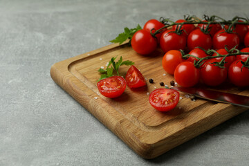 Cutting board with cherry tomato on gray textured background