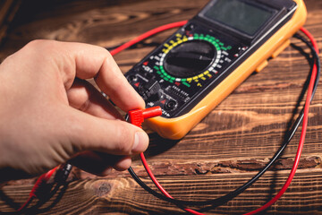 Multimeter and two test leads on a wooden background. A man's hand holds two test leads. A studio photo with hard lighting.