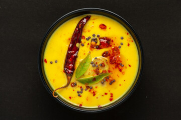 Close-up of Indian traditional kadhi or kadi pakora yogurt and gram flour and turmeric served hot in a black bowl. Over black background.
