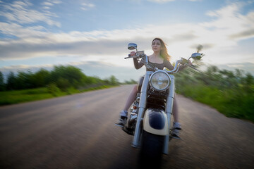 Attractive brunette motorcyclist with motorcycle in a summer evening during sunset. Adventure and travel concept.