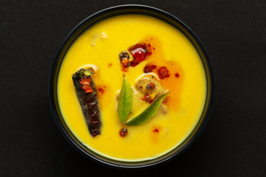 Close-up of Indian traditional kadhi or kadi pakora yogurt and gram flour and turmeric served hot in a black bowl. Over a black background.

