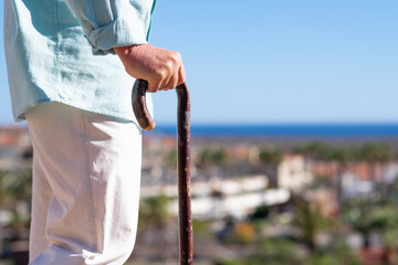 Close-up view of suffering elderly man walking with the help of a cane. Horizon over water