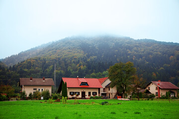 Fototapeta na wymiar Idyllic mountain village landscape with little houses with red roof and vast green lawns. Evening dusk time, after sunset, beautiful nature, blue mist on the hills. Outdoors, copy space.