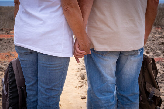 Back view of two mature people hand in hand in outdoor excursion in arid footpath