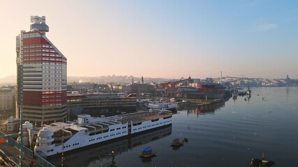 Tram Travelling At Gotaalvbron Bridge With P-Arken Ship On Harbour Beside Lilla Bommen Building At Sunrise In Gothenburg, Sweden. - aerial