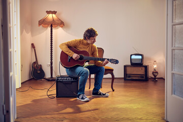 Male musician playing acoustic guitar on the amplifier in retro vintage room.