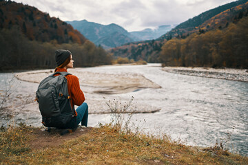 traveler sits on the banks of the river in the mountains in nature back view