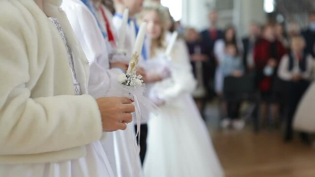 Children in smart dresses are at the first communion in the church. Children hold candles in their hands for the first communion.