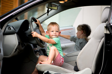 Two little cute children - a brother and a sister playing driving in the car at the wheel.