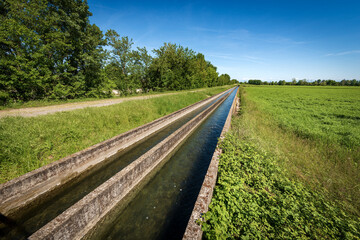 Fototapeta premium Two small concrete irrigation canals in the countryside, Padan Plain or Po valley (Pianura Padana, Italian). Mantua province, Italy, southern Europe.