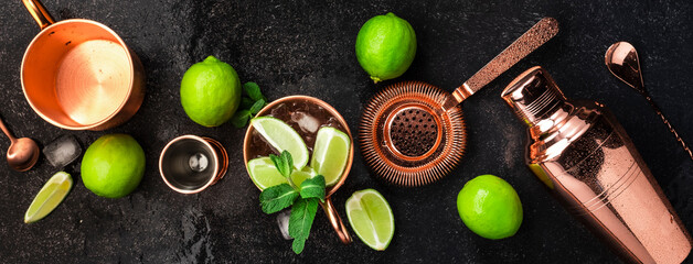 Moscow Mule. Preparation cocktail  with ginger beer, vodka, lime and ice. Copper bar tools. Black bar counter. Top view - obrazy, fototapety, plakaty