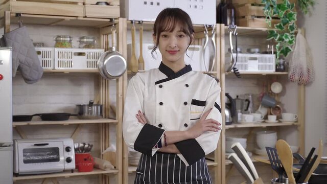 waist up, confident asian chef smiling at camera with arms crossed. background cozy home kitchen with wooden shelves. profession, profile picture concept