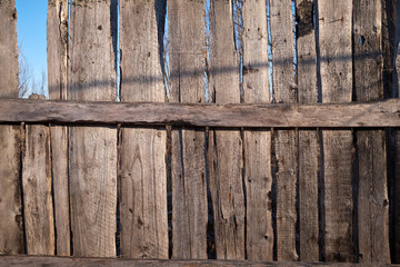 Old dilapidated wooden fence with rusty nails against the blue sky. Village background. Silence and desolation.