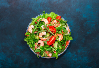 Shrimp salad with tomatoes, lettuce, arugula, avocado, cucumber and lemon dressing on blue table. Healthy eating, clean food concept. Top view
