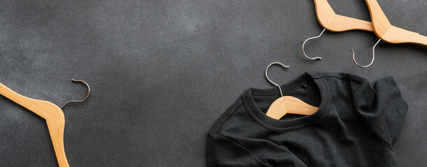 Gray T-shirt on wooden hanger. Black stone background, top view. Clothing sale concept, fashion...