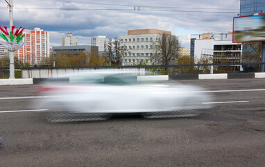 The movement of a blurred white car along the overpass in the daytime.