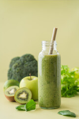 Green smoothie in glass bottles with bamboo tubes. Broccoli, celery, apple, kiwi, lime, spinach smoothies on the green background