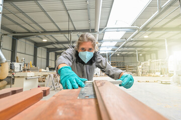 Woman worker operating in the carpentry workshop  and wearing protections againt covid-19