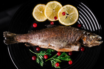 oven-baked fish with lemon on a black plate top view. grilled dorado