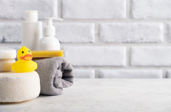 Baby hygiene accessories in home bathroom. Rubber toy, cosmetic cream, soap, sponge, shampoo bottle and towel. Copy space, close up