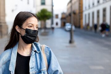 Fototapeta premium Young woman with surgical mask. She is on the street, a white girl with brown hair. There is natural light from the sunset. She is in the historic center of Vegueta, Las Palmas de Gran Canaria, Spain.