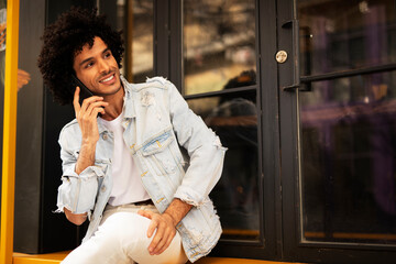 Young man drinking coffee outdoors. Handsome man with curly hair talking to the phone.