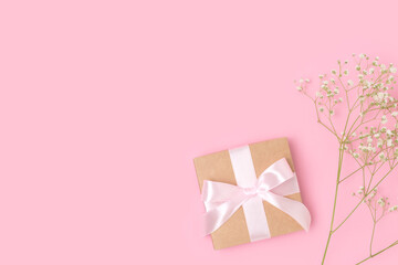 Present with a tied ribbon and branch of gypsophila flower on a pink pastel background. Gift for springtime holidays with copyspace.