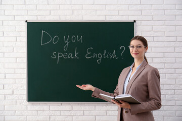 Teacher near green chalkboard with inscription Do You Speak English? in classroom
