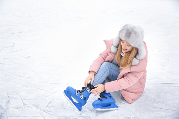 Woman adjusting figure skate while sitting on ice rink. Space for text