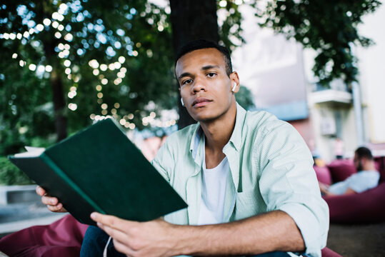 Young African American guy sitting with notebook in garden with garland