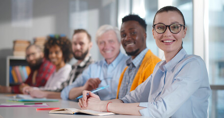 Multiethnic smiling people sitting at desk and looking at camera