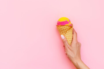 Sweet yellow pink fruit ice-cream sorbet in a waffle cone with banana and strawberry flavor in a woman's hand isolated on a light color pink background. Copy space for text or design. Summer concept