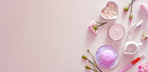 Natural cosmetics with floral scent on a pink background banner. Bath salt, aromatic bomb, oils, cream, serum, flower petals, top view, flat lay, copy space. Floral cosmetics background