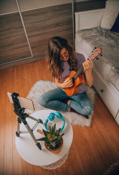 Online ukulele lessons. A modern woman watches video tutorials/learn students how to play instrument online.