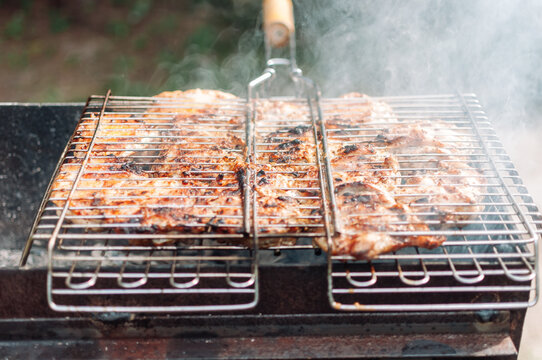 Grilled chicken thighs marinated in sauce and spices. Juicy cuts of meat marinated with smoke rising from charcoal. Fried chicken kebab over an open fire. Campfire cooking season.