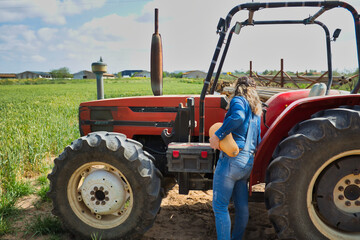 Blonde woman in jeans with a large organic pumpkin under her arm next to a tractor in from of a wheat field