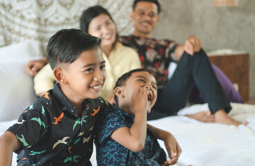 Southeast Asian family spending time at home. Happy Indonesian parents and children laying in bed having fun together