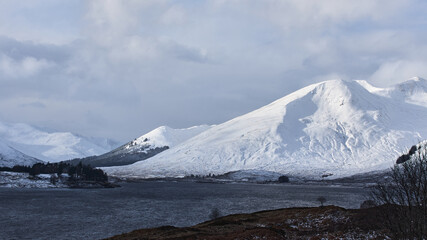 snowy landscape with large mountains in Scotland and lake. cloudy sky