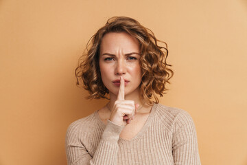 Displeased ginger woman with wavy hair showing silence gesture at camera