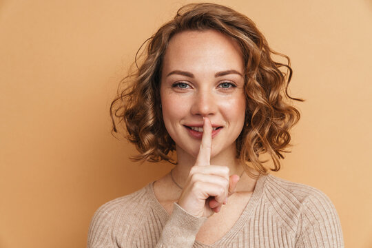 Smiling ginger woman with wavy hair showing silence gesture at camera