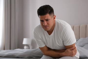 Man suffering from stomach ache on bed at home, space for text Food poisoning