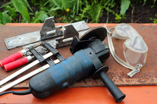 Angle grinder, safety goggles, f-clamps. Hand power tools, metalworking concept.