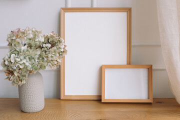 Blank white empty picture frames mockup and modern ceramic vase with dry hydrangea on wooden table....