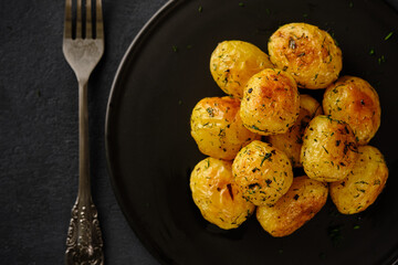 Pierced young potatoes in the oven with spicy herbs and garlic on a black background