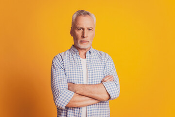 Self confident man keeps hands crossed looks at camera isolated over yellow background