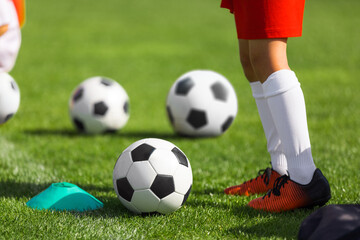 Close-up image of soccer kid in cleats and soccer uniform. Classic football balls on grass field