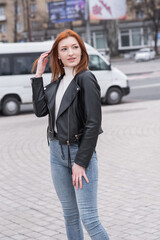Portrait of a beautiful and serious redhead woman with clothing in a grunge style. Posing while walking